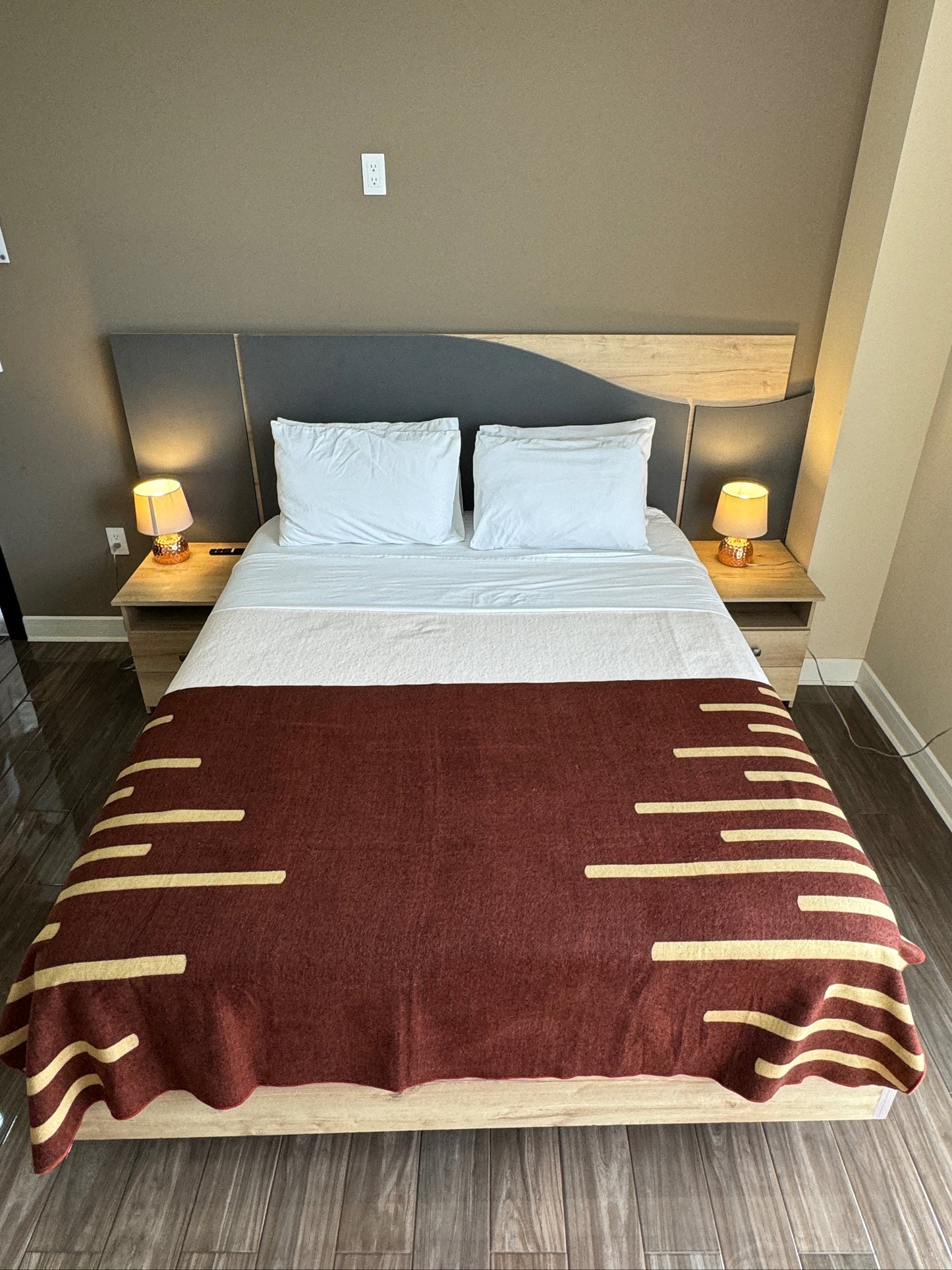 Bedroom with a bed featuring a red and gold striped blanket, two nightstands with lamps, and a gray headboard.