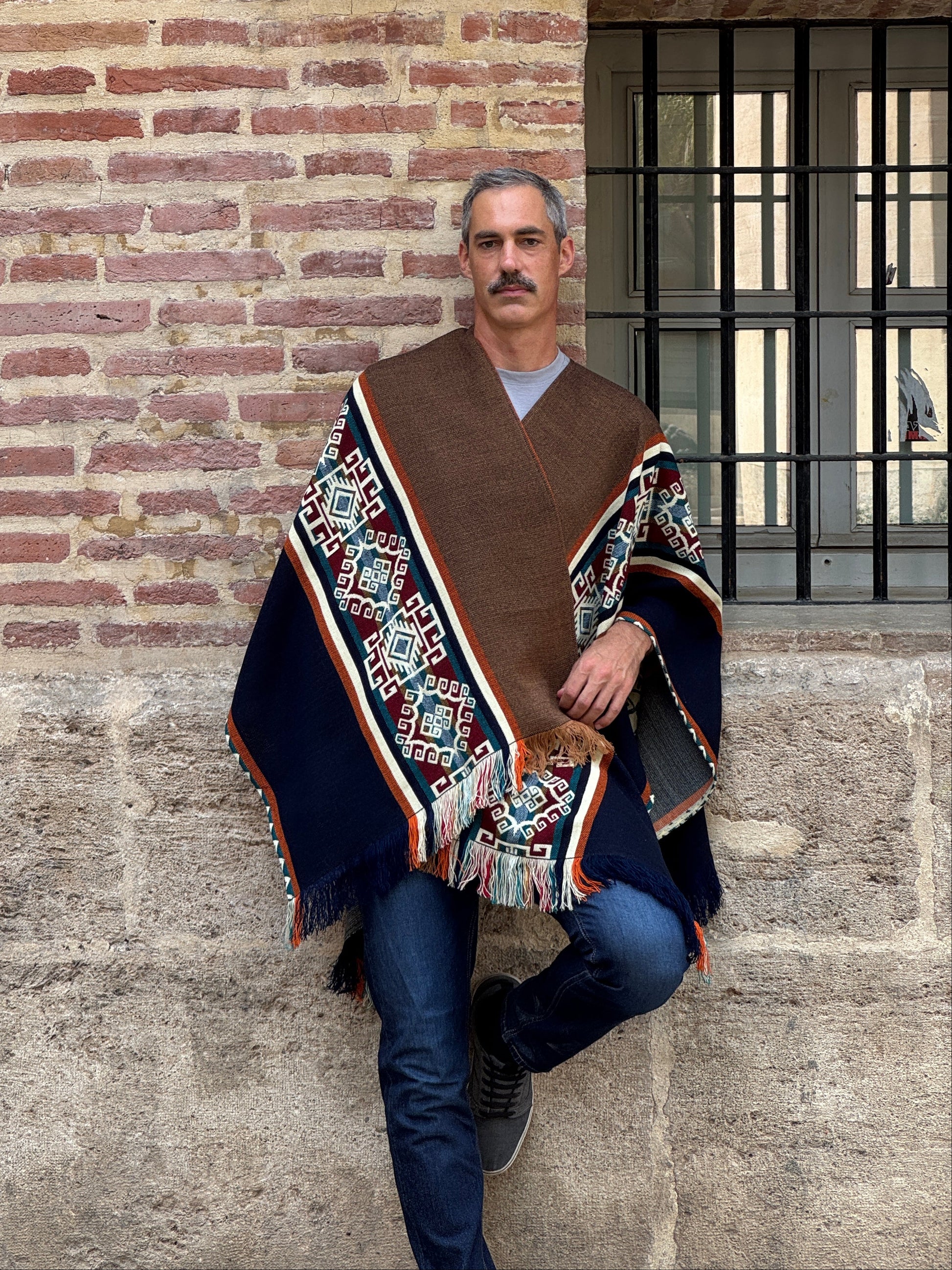 Man wearing a patterned jacket standing on a stone floor with a brick wall background