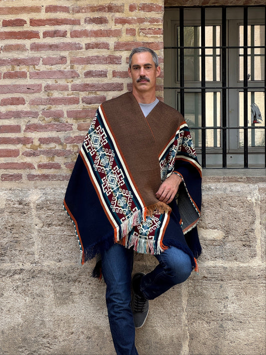 Man wearing a patterned jacket standing on a stone floor with a brick wall background